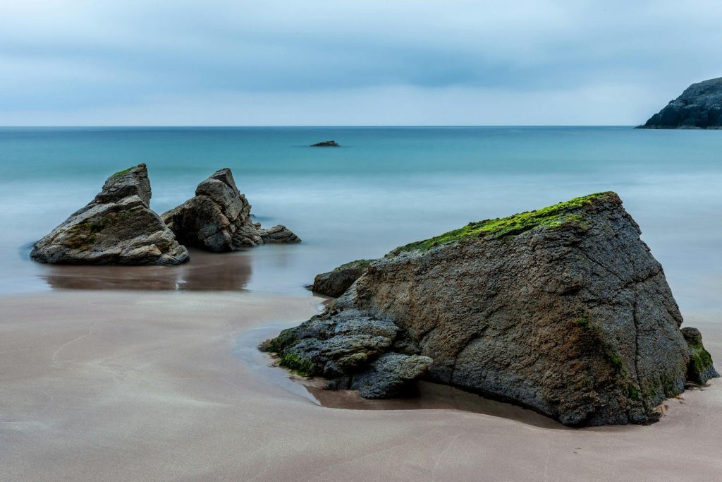 Peaceful beach with rocks and gentle waves under a cloudy sky.